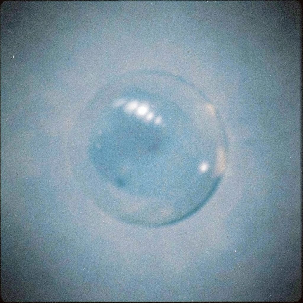 Floating soap bubbles drifting across a pale teal sky, light and airy with gentle film grain